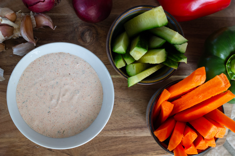 Dipmix med løg, hvidløg, dild og paprika, og gulerødder, agurker og peberfrugt i skåle.